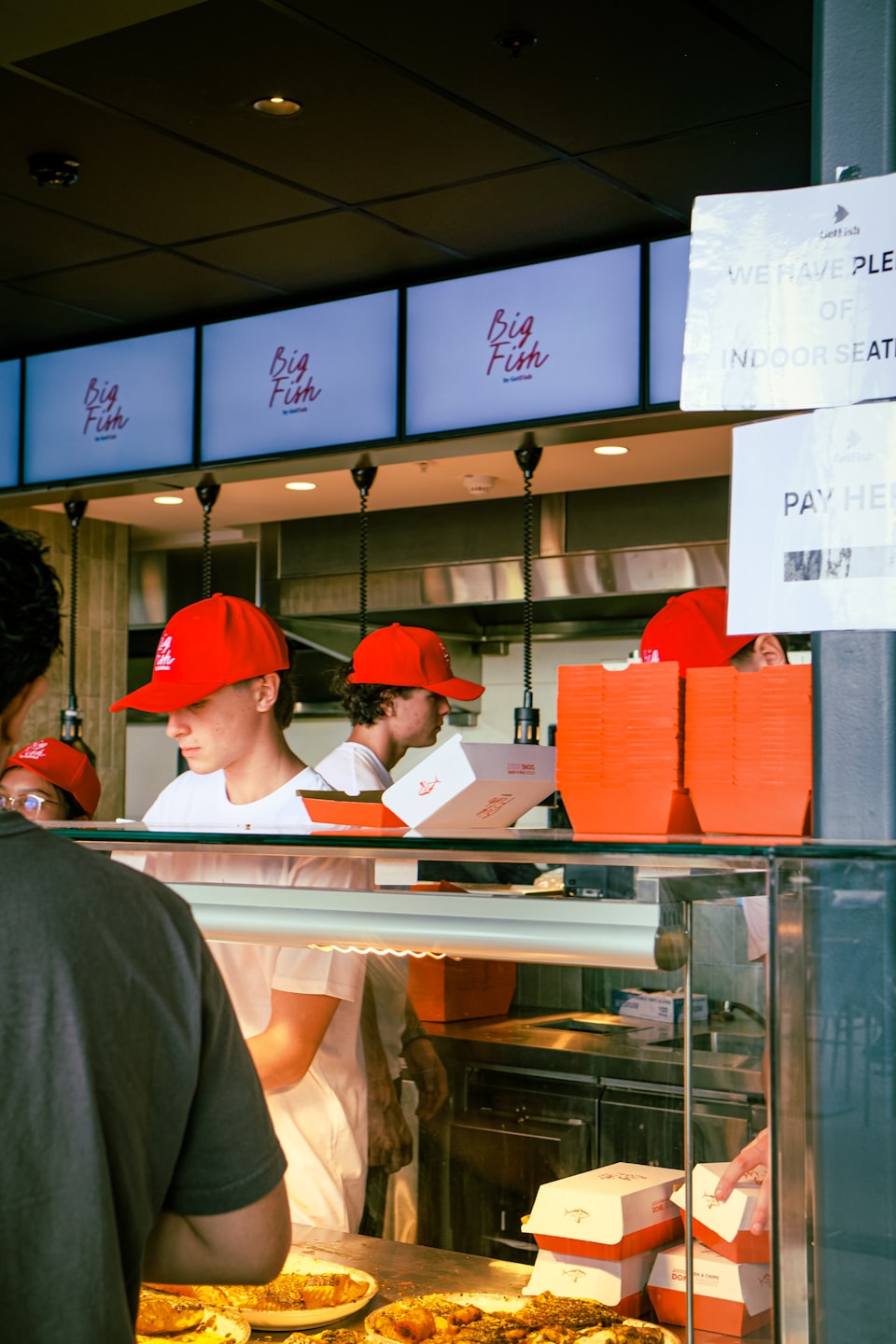 Employees in red caps serving customers at a restaurant counter.